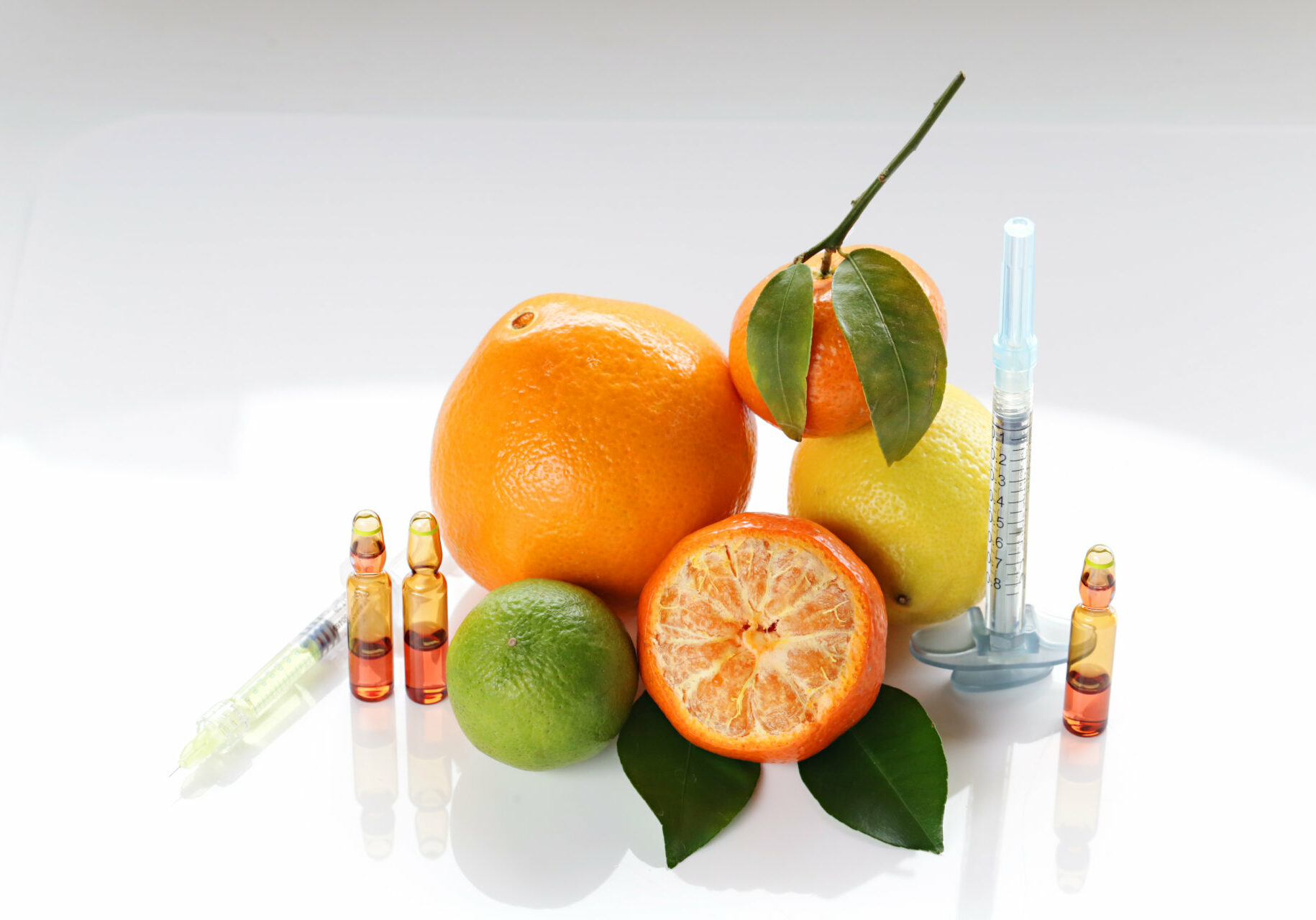 Vitamin C in ampoules, two syringes, mandarin, lemon,  orange and lime on a light background.  Cosmetics Concept